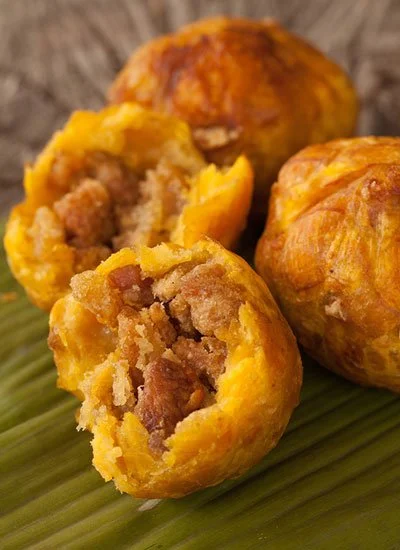 Close-up of three cooked meat-filled dumplings or fried balls on a green leaf.