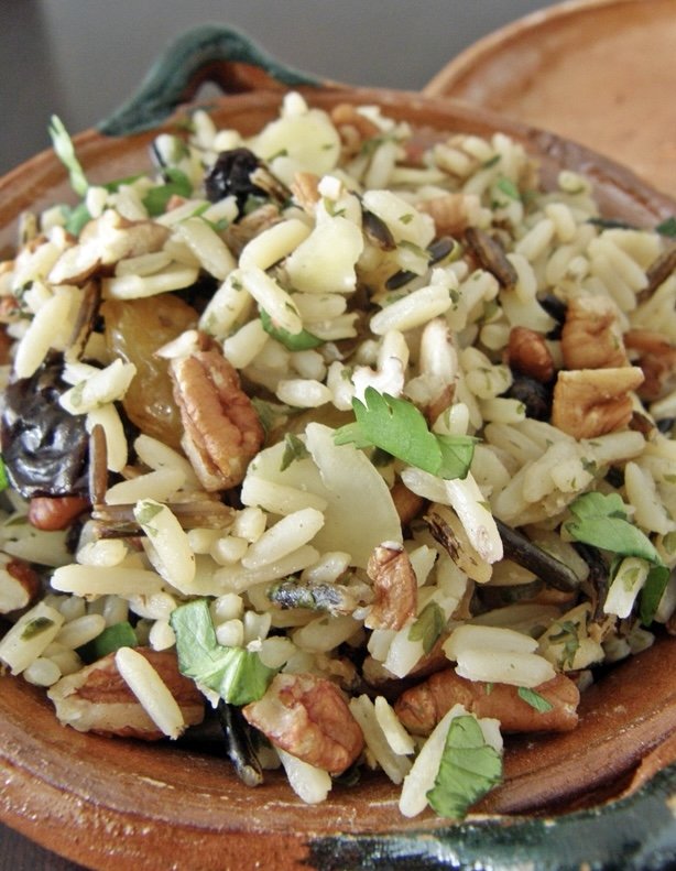 Close-up of a rice salad with nuts, herbs, and dried fruits in a wooden bowl.