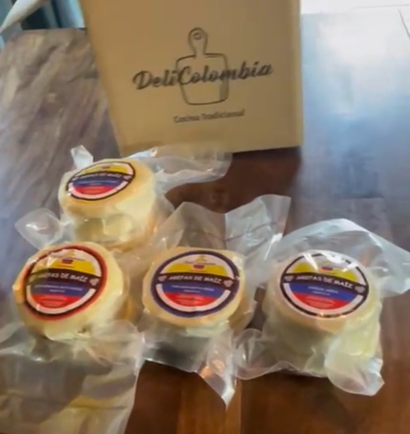 Four small, circular blocks wrapped in plastic with labels, placed on a wooden surface in front of a paper bag with a logo and text. The labels are in Spanish.