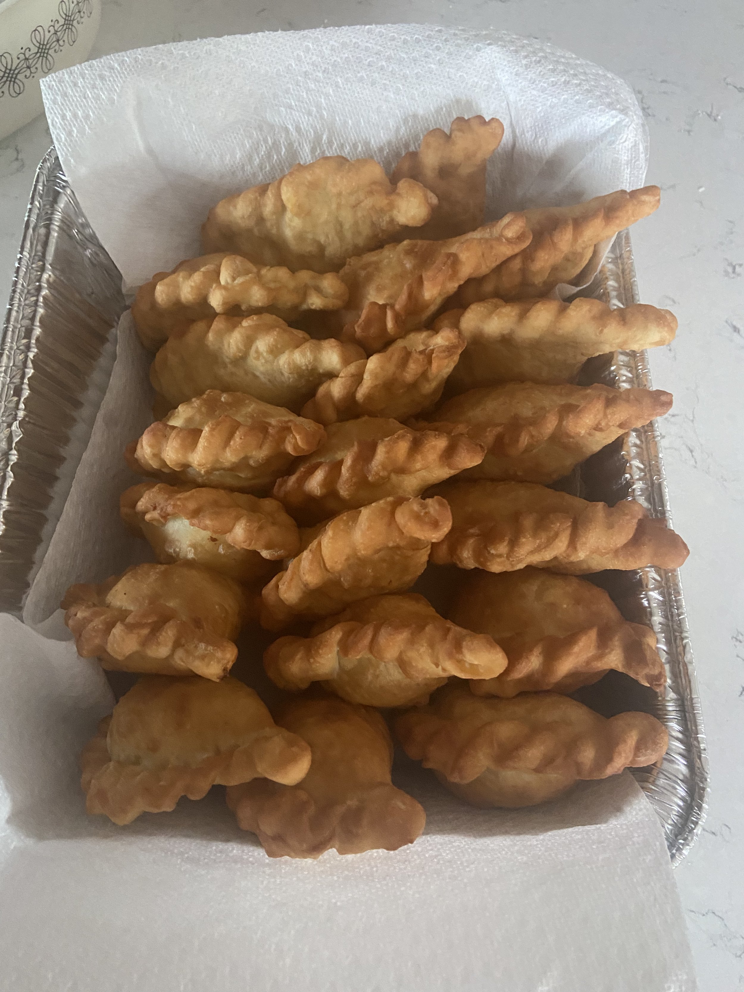 A tray of deep-fried Asian snacks, including empanadas and chebureks, lined with paper towels for cooling.