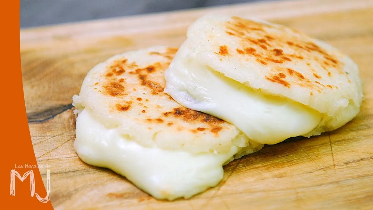 Close-up of two cheese arepas on a wooden cutting board.