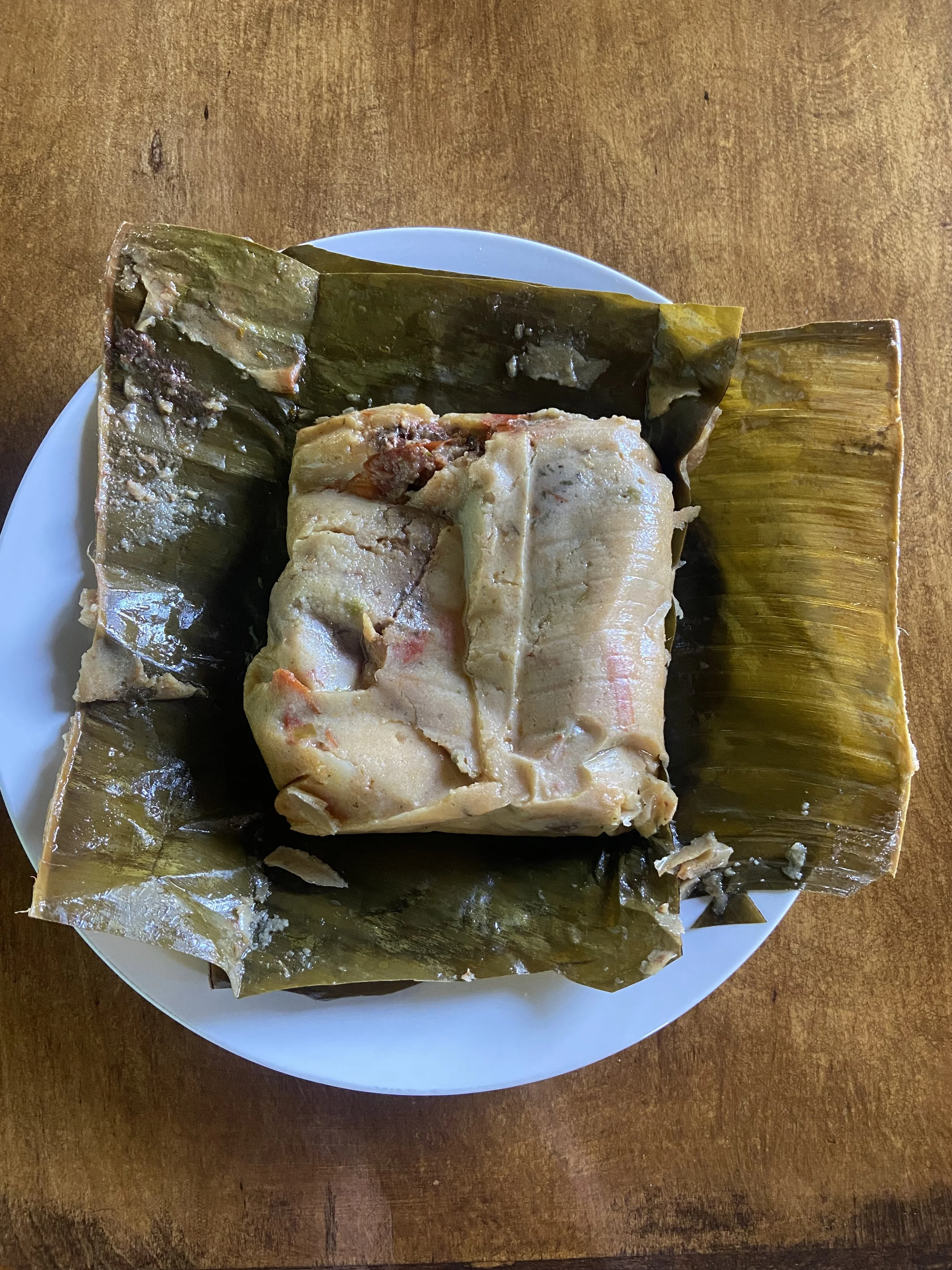 A traditional Asian dish with fish and rice wrapped in banana leaves on a white plate.