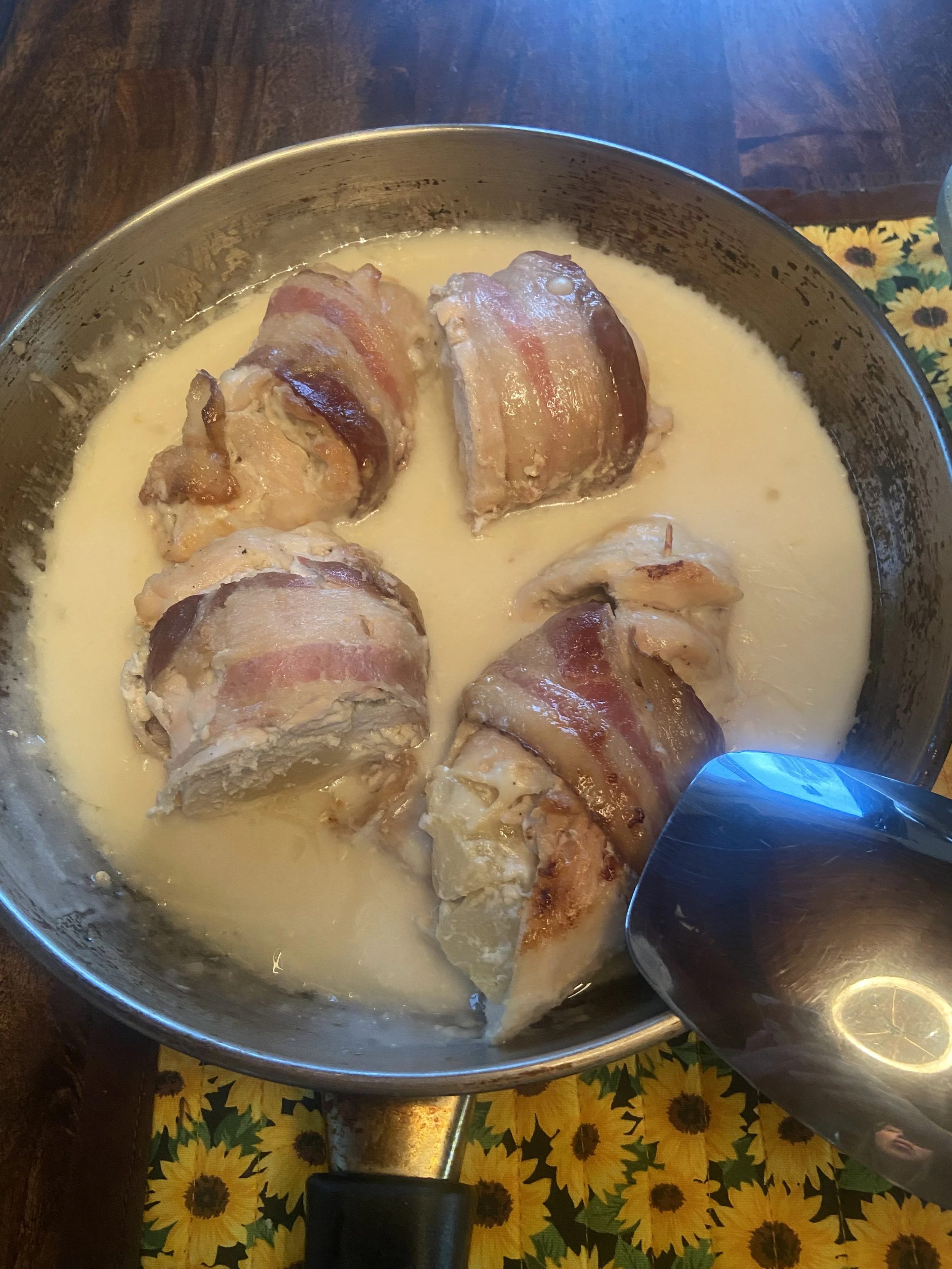 Four pieces of bacon-wrapped chicken in creamy white sauce in a skillet.