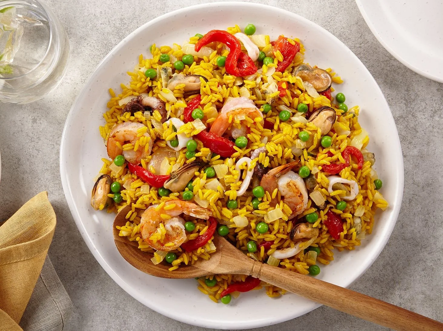 A white plate with yellow rice, shrimp, squid, green peas, red bell peppers, and onions.