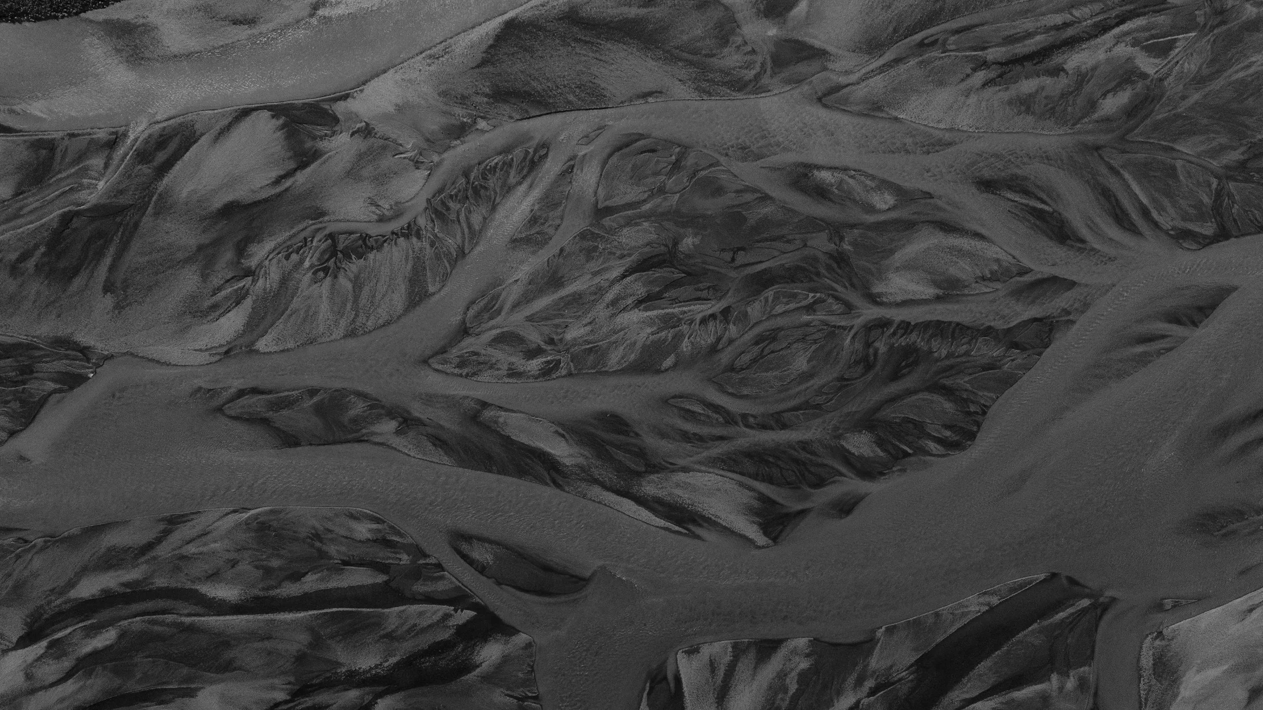 Black and white aerial view of a landscape with winding rivers and textured land formations.