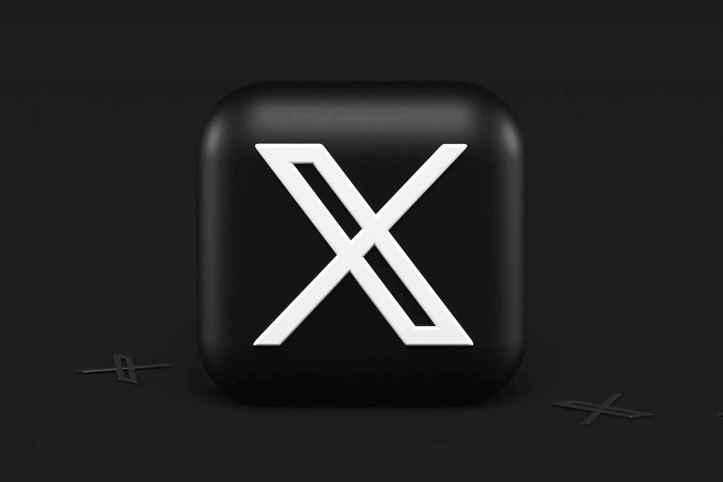A black rectangular sculpture with rounded edges features a white illuminated 'X' design on its front surface, set against a black background with various black 'X' shapes on the ground.