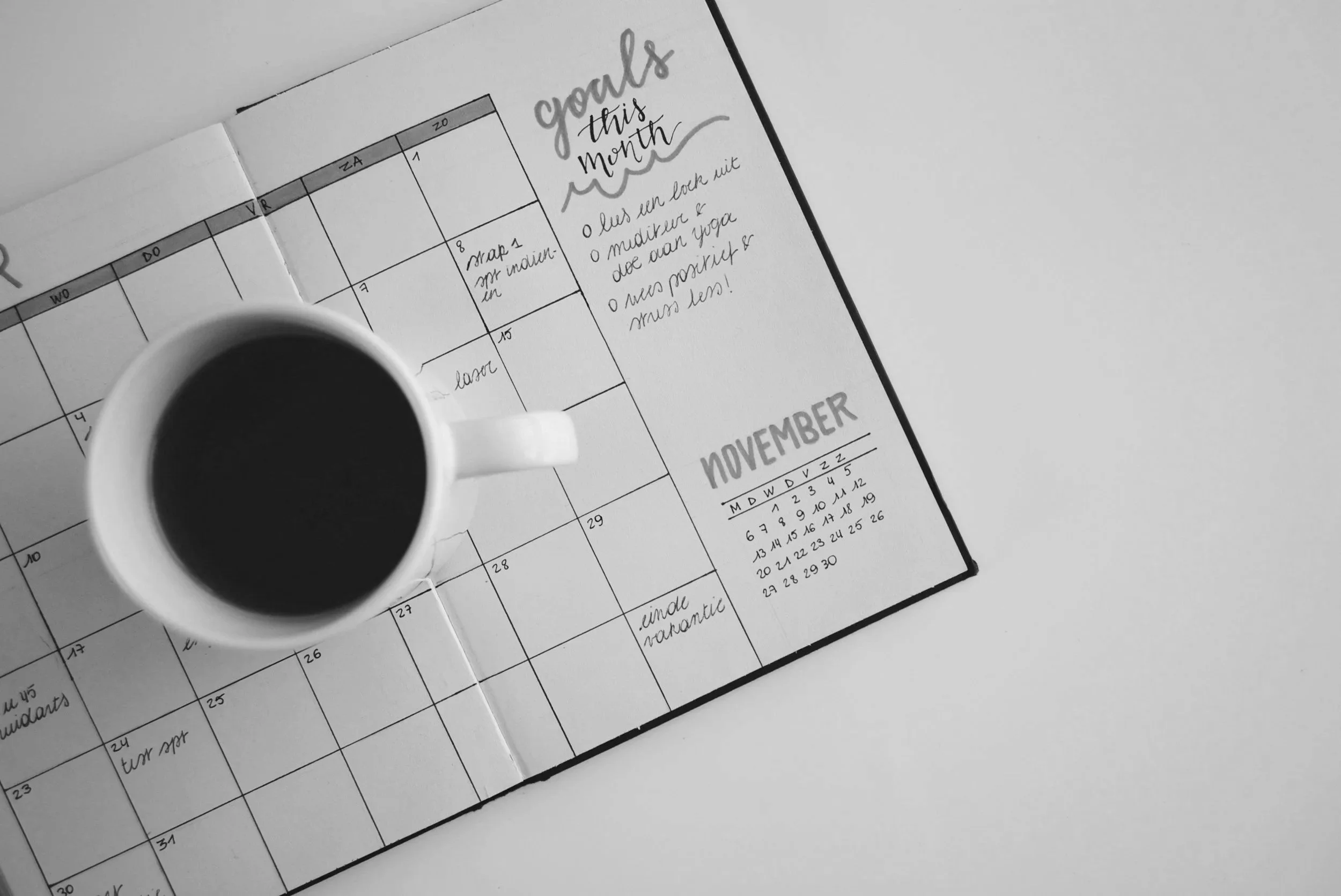 Black coffee in a white mug placed on an open planner with handwritten notes and a small calendar for November.