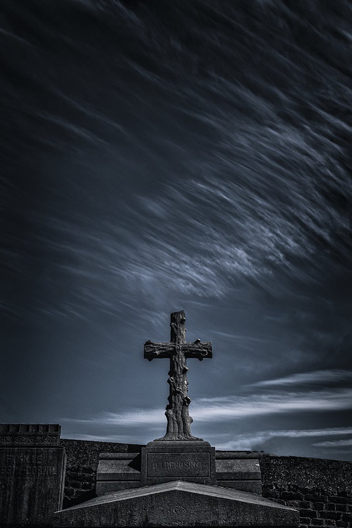 Croix en bois ancienne sur une tombe, ciel orageux sombre.