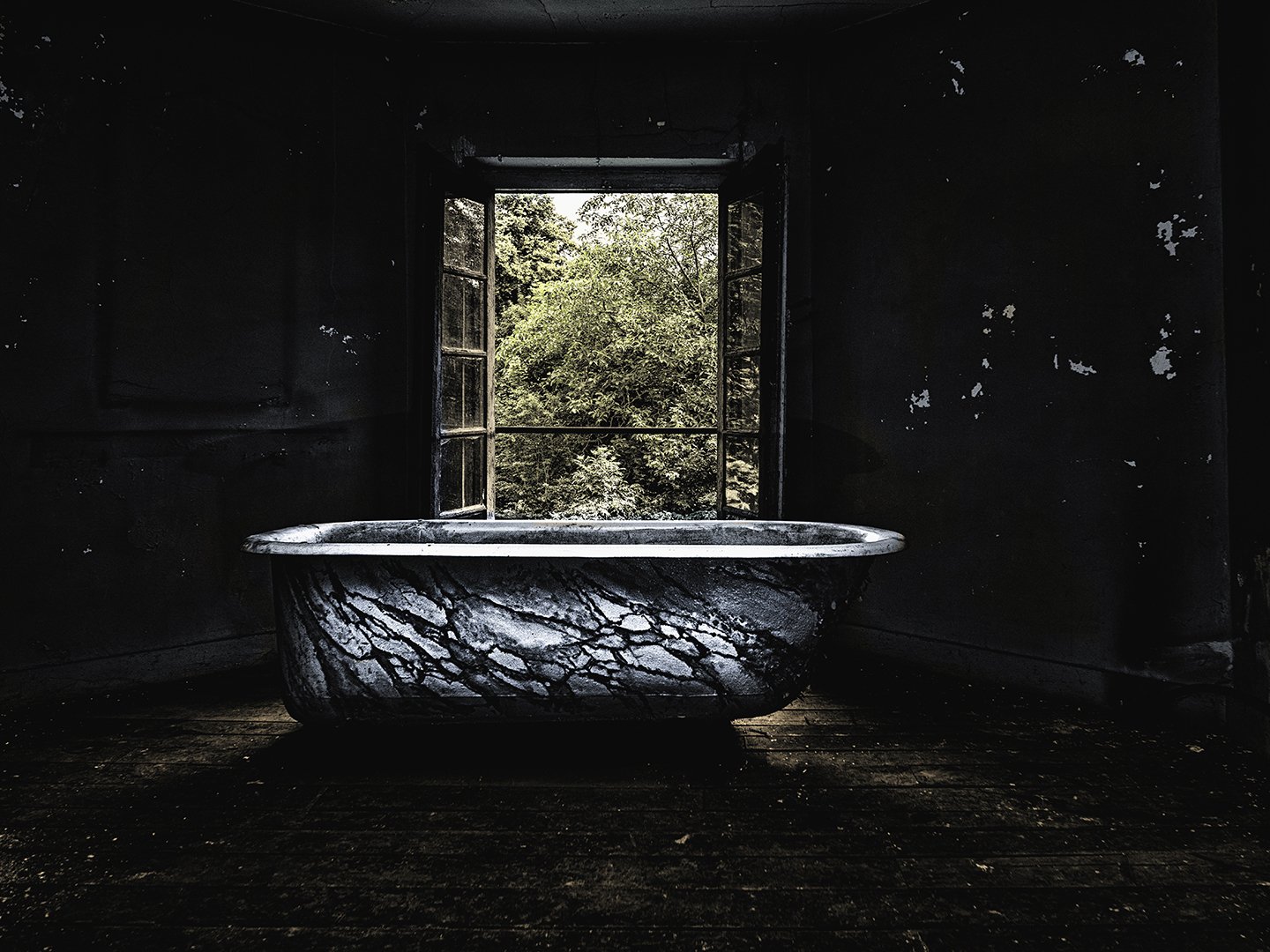 Une baignoire en marbre dans une pièce sombre, avec une fenêtre ouverte laissant voir des arbres verts à l'extérieur.