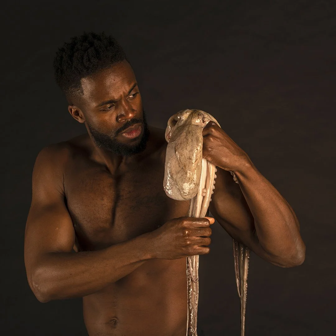 Un homme nu tient une grande pieuvre avec une expression inquiète ou concentrée.