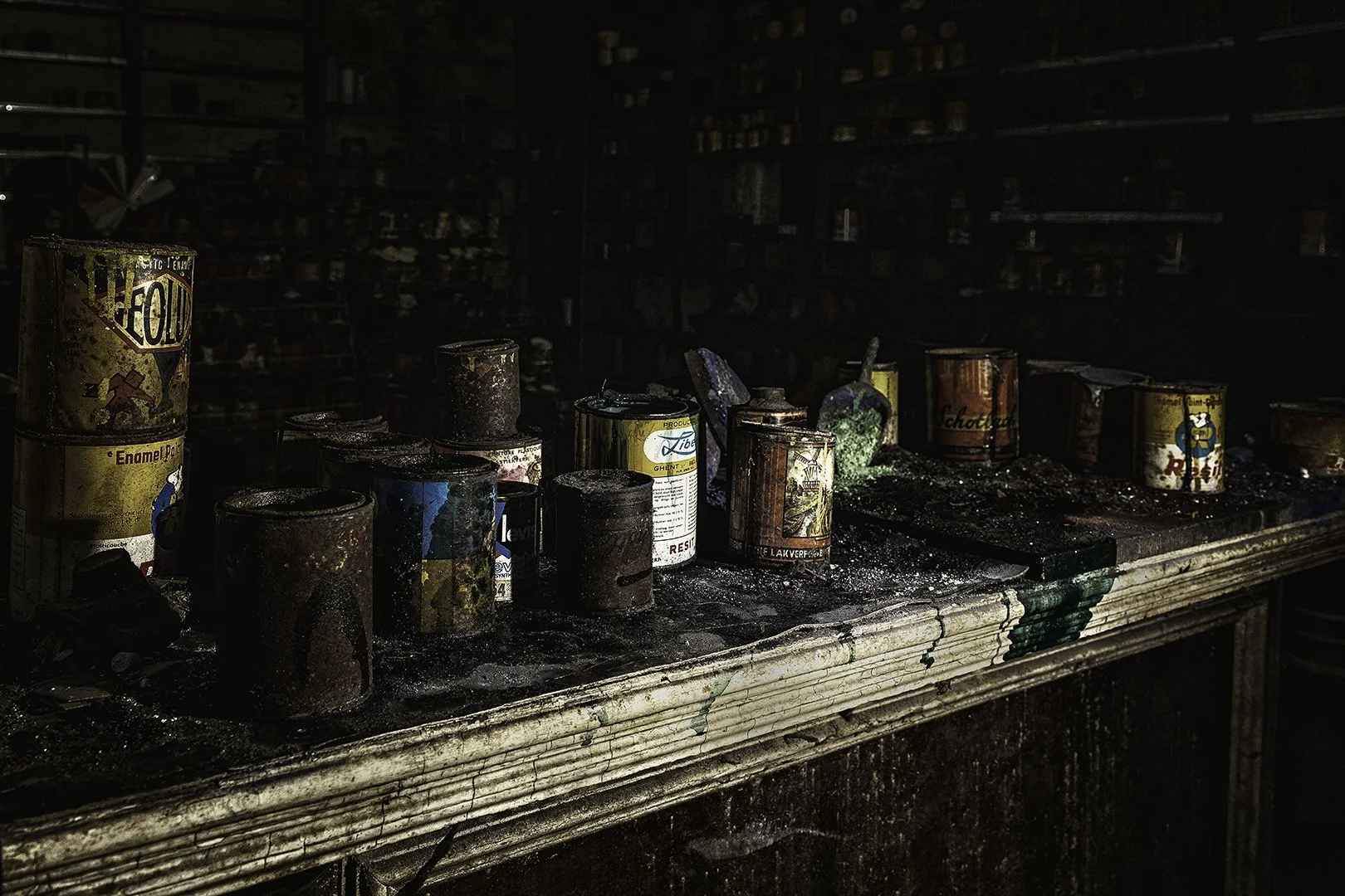 Vieux pots de peinture rouillés sur un comptoir en bois dans un lieu abandonné ou endommagé par un incendie.