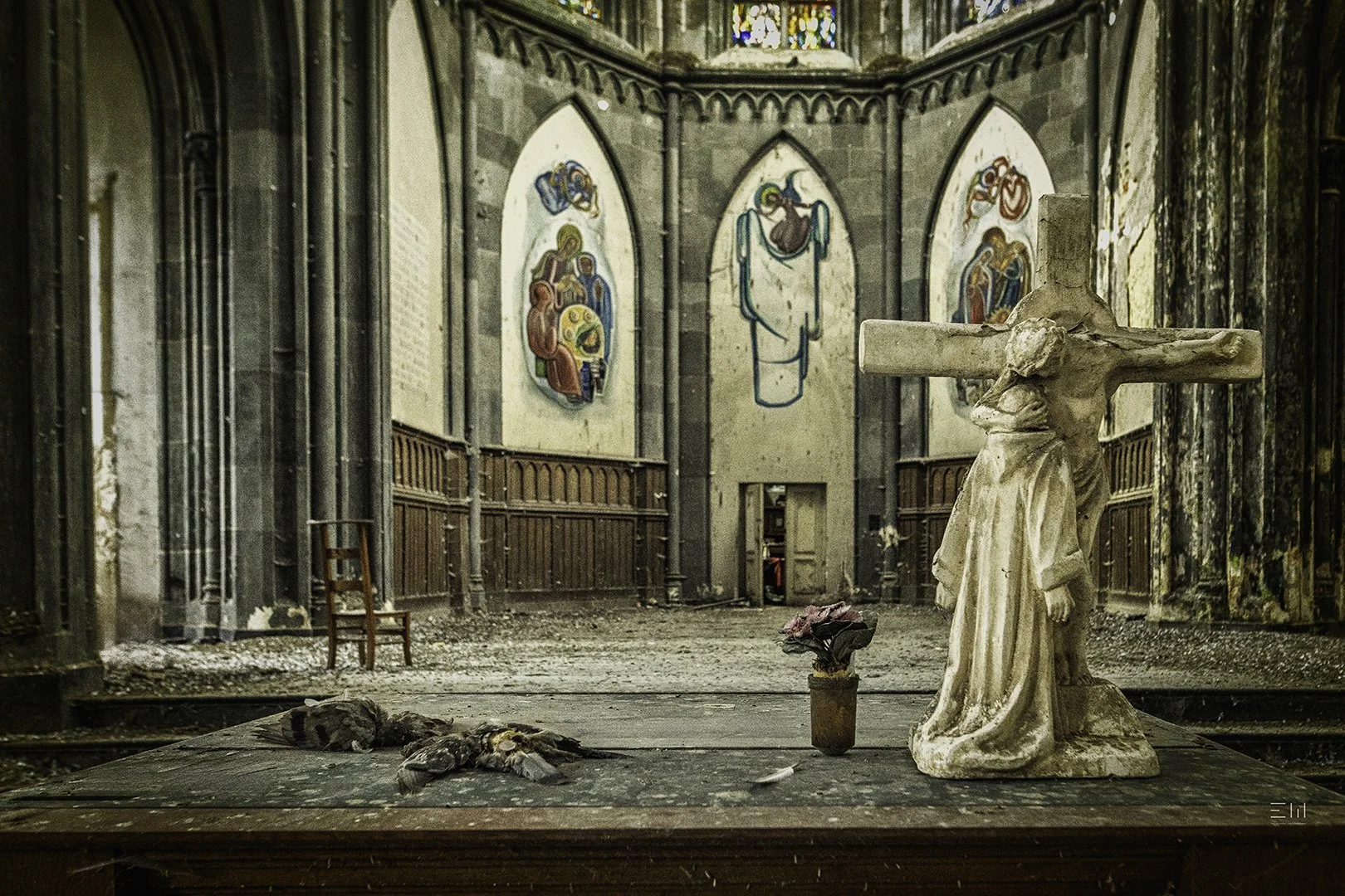 Une scène de l'intérieur d'une vieille église abandonnée, avec une croix en pierre, une fleur fanée dans un vase, un nuage de poussière, une simple chaise en bois et des vitraux colorés usés en arrière-plan.