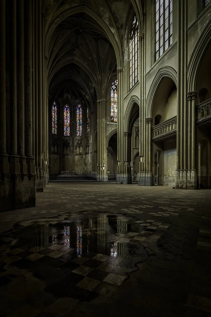 Intérieur d'une ancienne cathédrale gothique avec des vitraux colorés et de hautes arches en pierre.