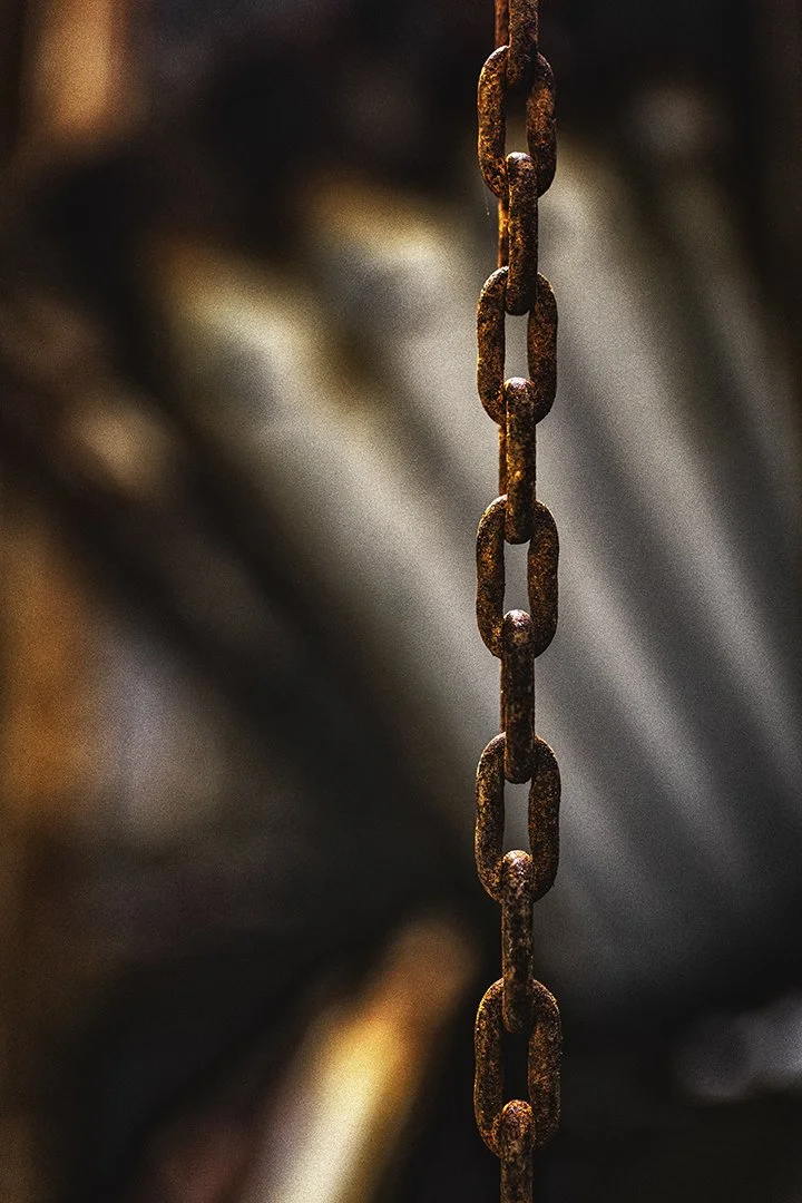 Chaîne en métal rouillée suspendue, avec un fond flou et sombre.
