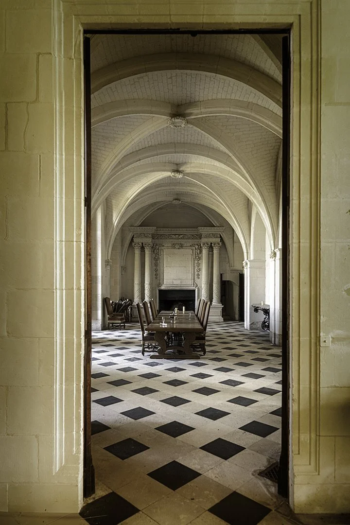 Salle à manger élégante avec un plafond voûté en pierre et un sol à carreaux noirs et blancs, vue à travers une porte.