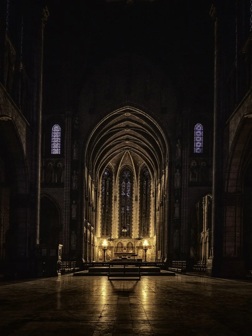 Intérieur d'une grande église gothique avec un autel iluminé, des vitraux et des arches en pierre