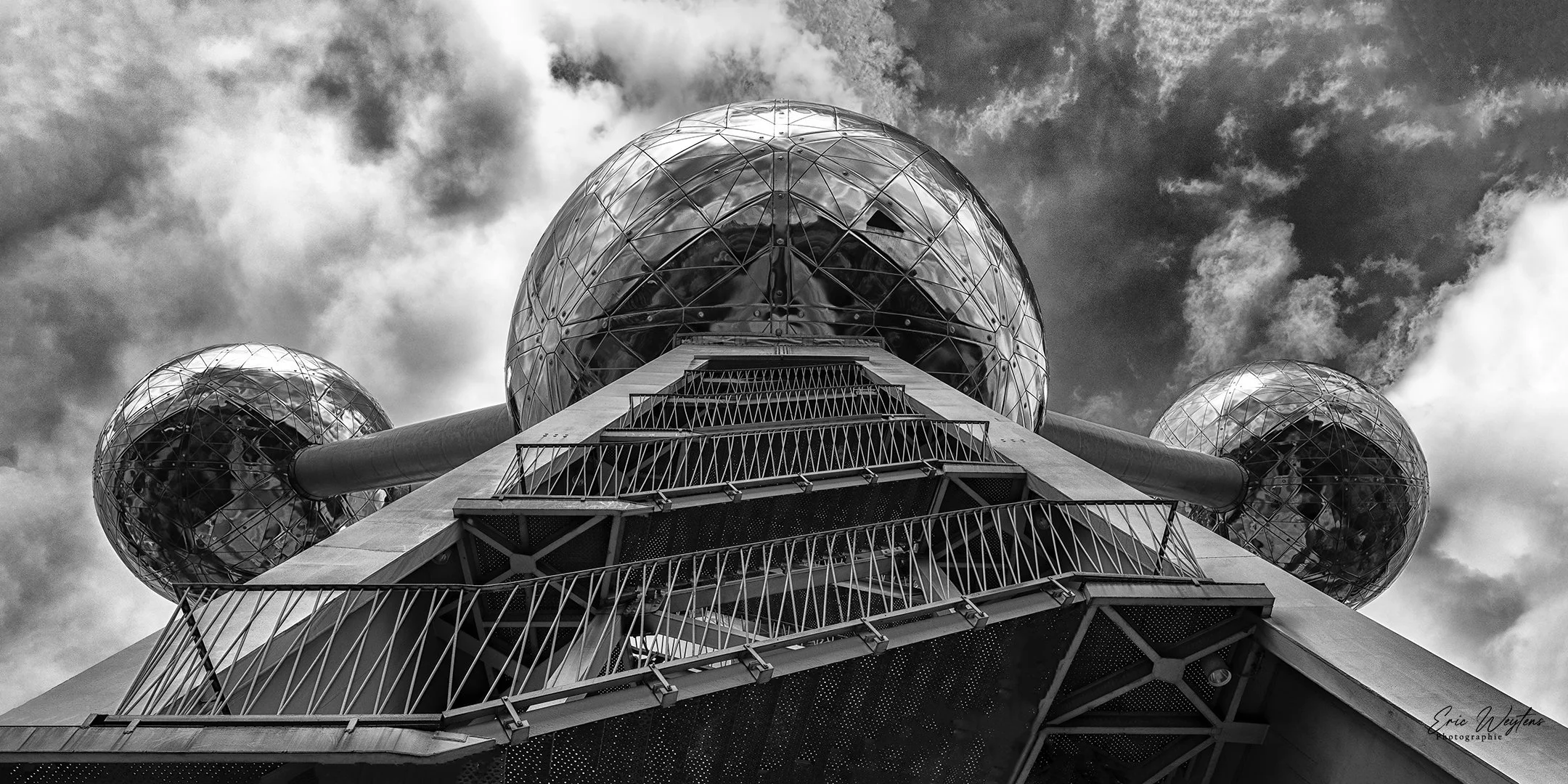 Une vue en contre-plongée de la biénerie atomique de Bruxelles avec ses sphères métalliques réfléchissantes dans un ciel nuageux.