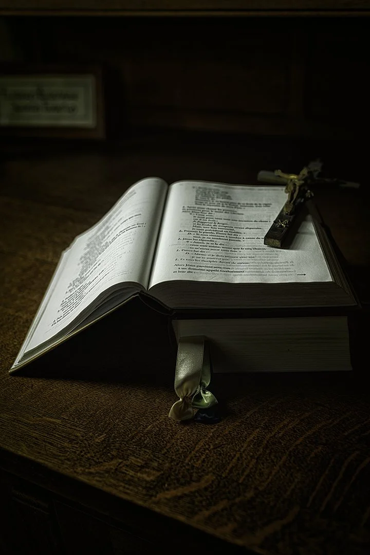 Une Bible ouverte posée sur une table en bois, avec une croix en bois posée dessus.