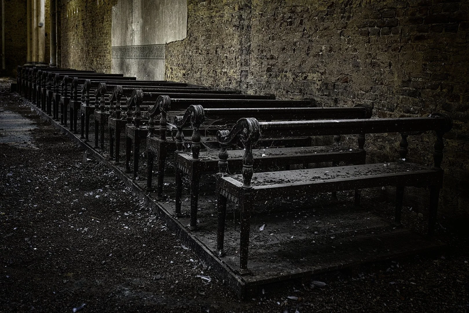 Bancs en bois abandonnés et couverts de poussière et de débris, situés contre un mur en briques dans un endroit abandonné.