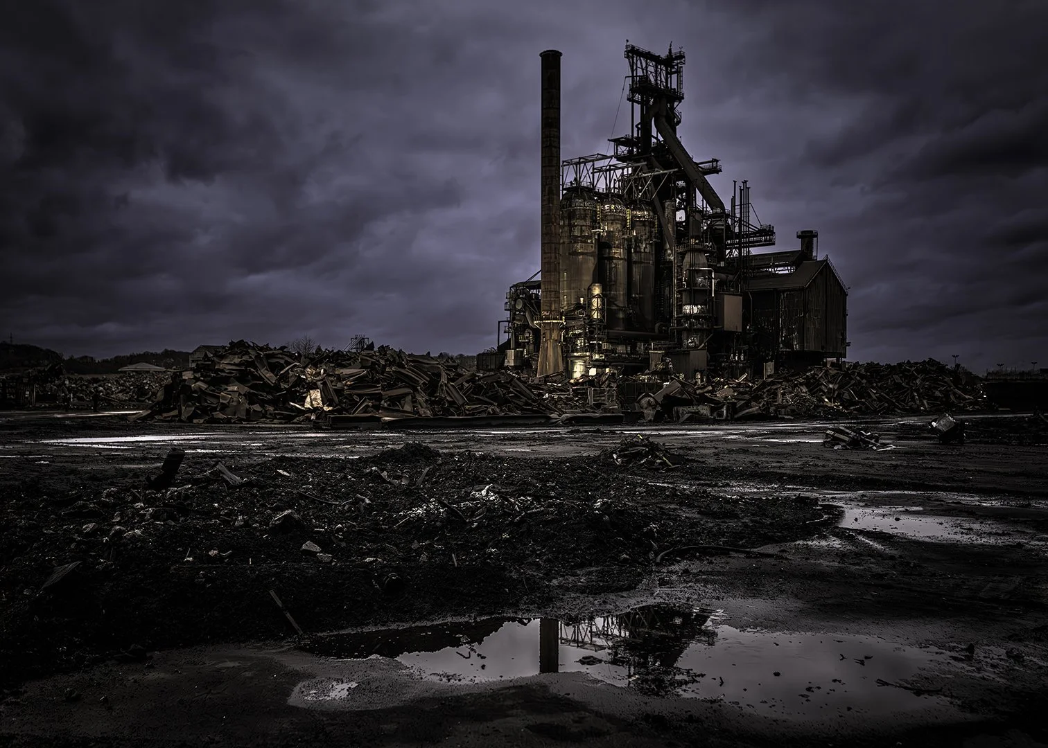 Une centrale électrique désafectée sous un ciel orageux, avec un sol noir et des débris.