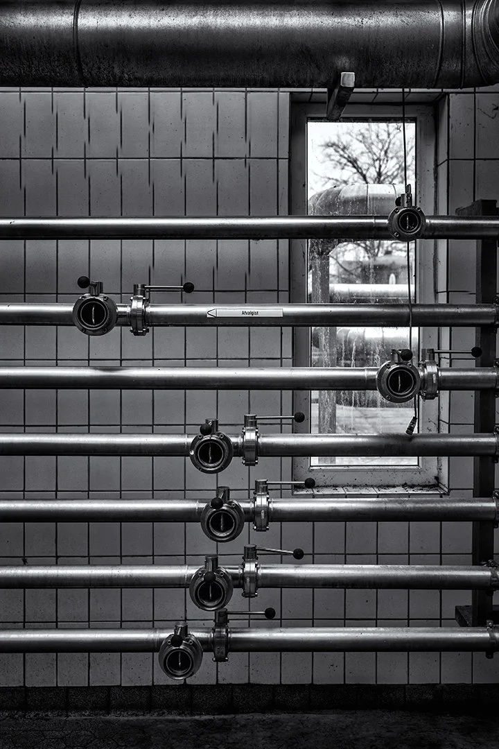 Tuyaux en acier inoxydable fixés au mur en céramique avec un tuyau d'échappement noir au plafond, vue d'une fenêtre avec un arbre dehors.