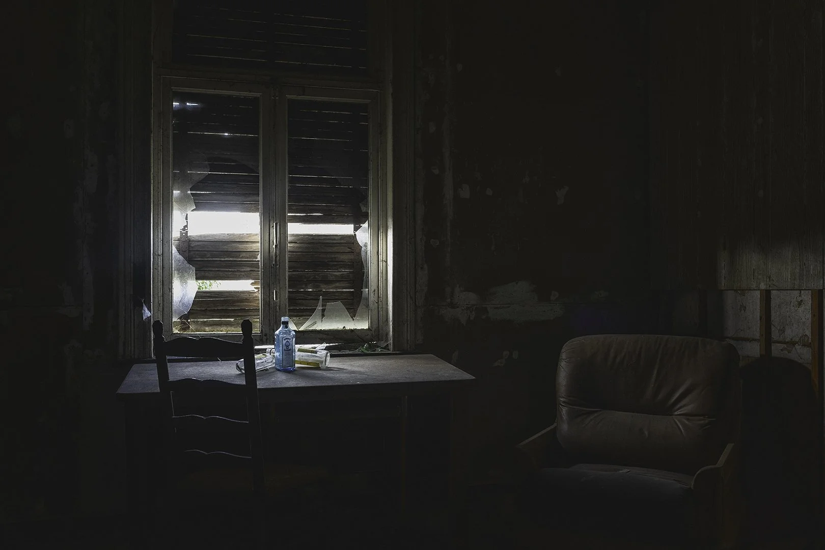 Une pièce sombre avec une fenêtre cassée, une table avec une bouteille d'eau et une armure.