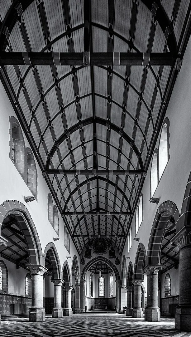 Intérieur d'une vieille église ou cathédrale avec des voutes en métal, arches, colonnes en pierre et fenêtres en arc.