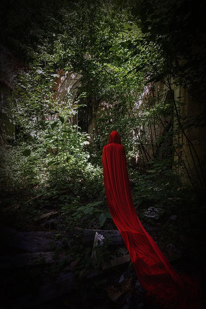 Une personne portant un long voile ou cape rouge dans une forêt dense avec des feuillages verts.