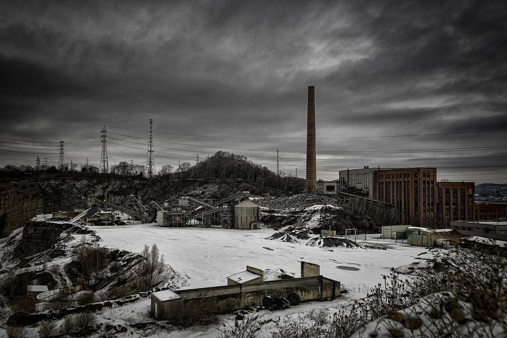 Une vue d'une vieille centrale électrique abandonnée sous un ciel nuageux, avec de la neige sur le sol.