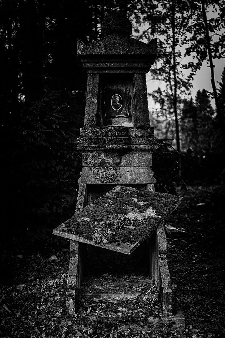Une vieille stèle funéraire abandonnée dans une forêt, recouverte de feuilles et de débris.