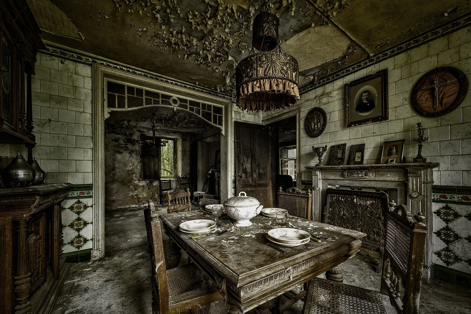 Une salle à manger ancienne, en désordre, avec une table en bois autour de laquelle sont placés des assiettes et des verres. L'intérieur est en mauvais état, avec un plafond endommagé, des murs en pierre, et des décorations anciennes, y compris des p