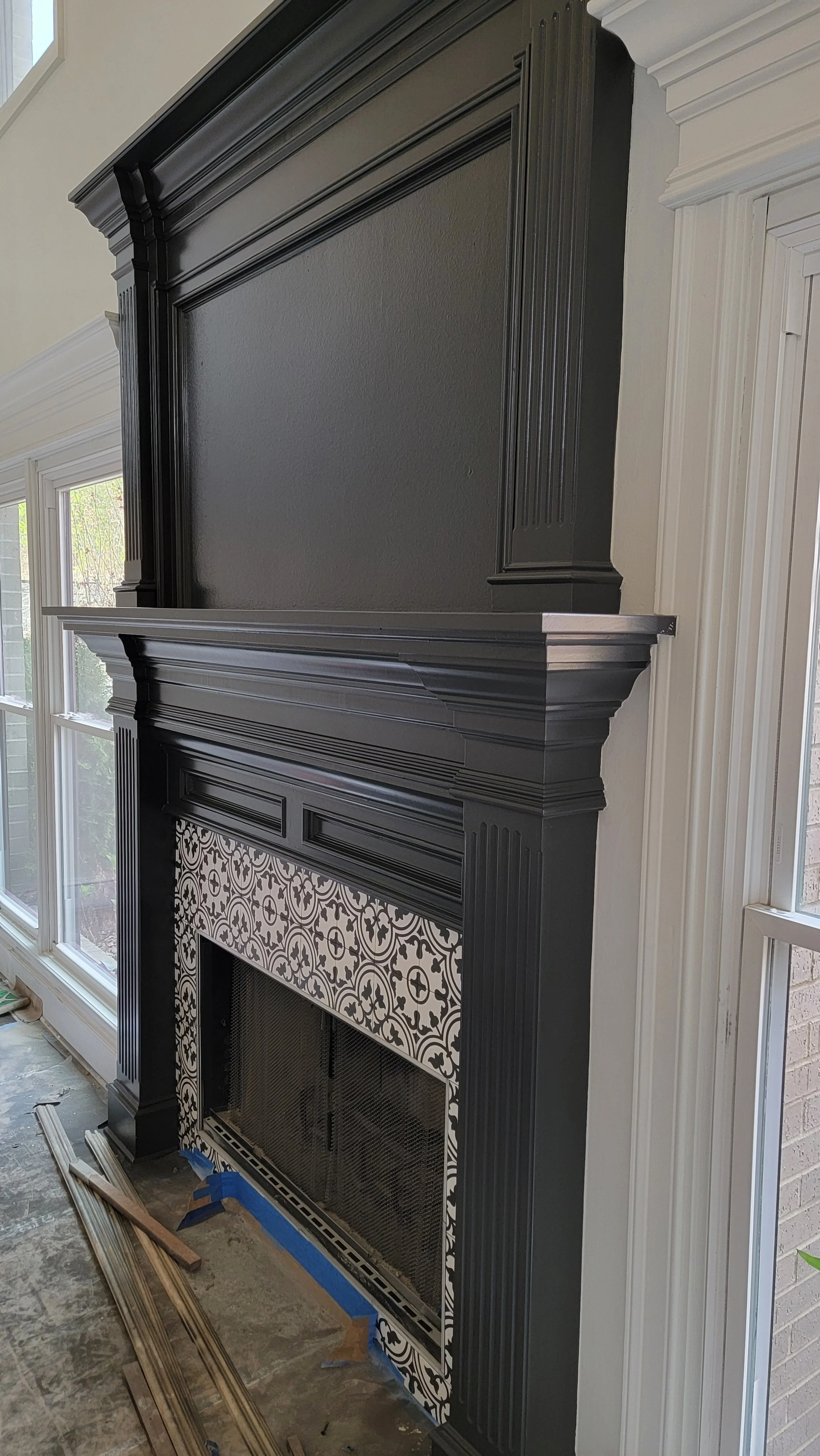 Black decorative fireplace mantel with patterned tile surround and white molding, located between two windows