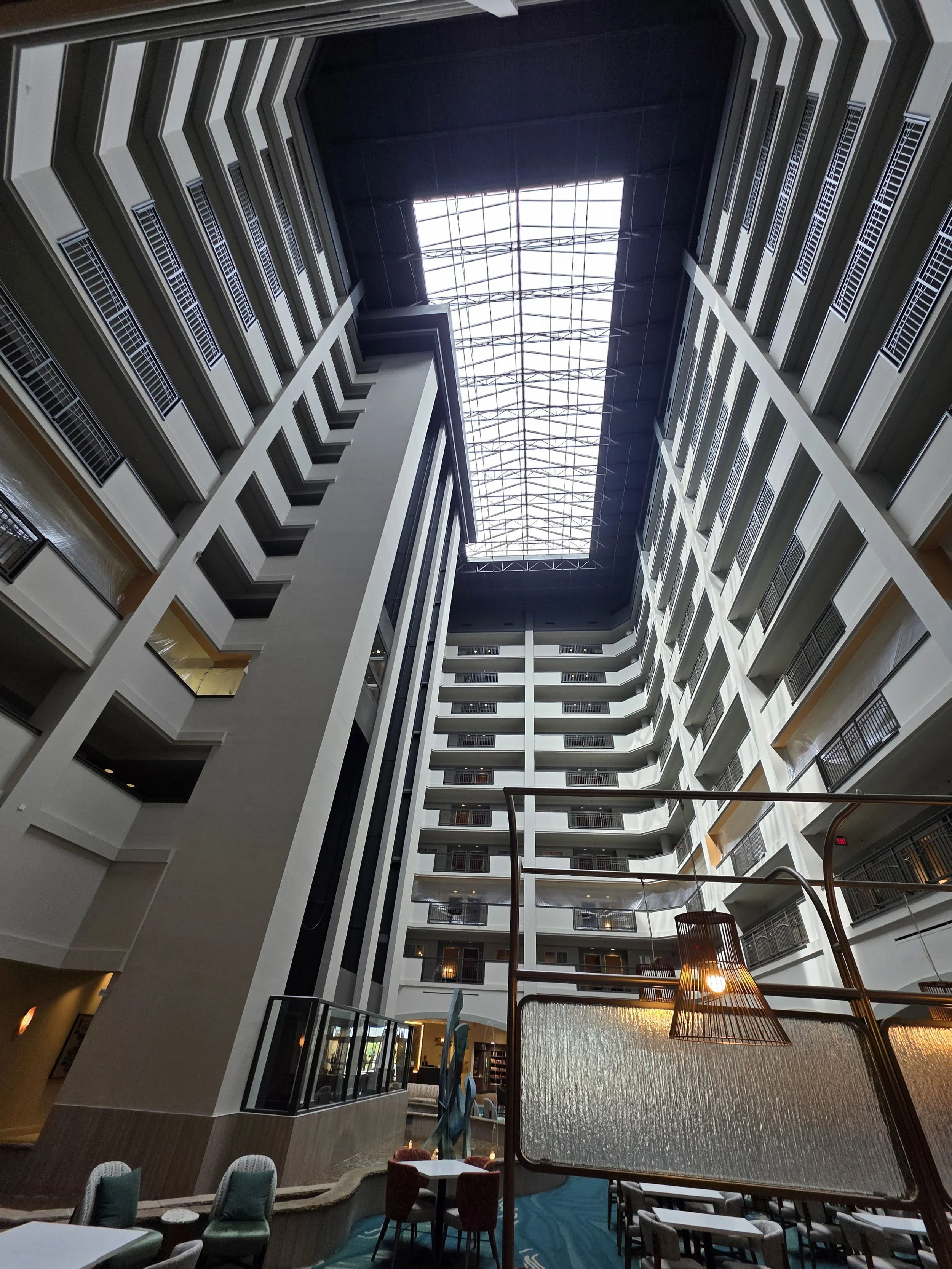Interior view of a tall atrium with multiple floors, balconies, and a large glass skylight ceiling.