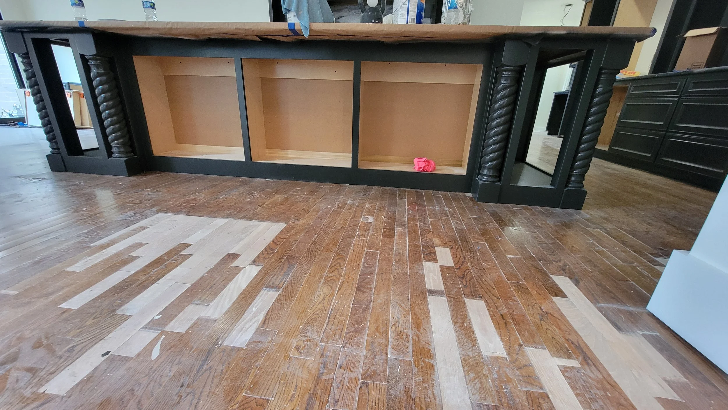 Wooden cabinet with open shelves and twisted column design on the sides located on a hardwood floor in a store. A pink cloth is on the bottom shelf. Part of a mirror and other furniture pieces are visible around.