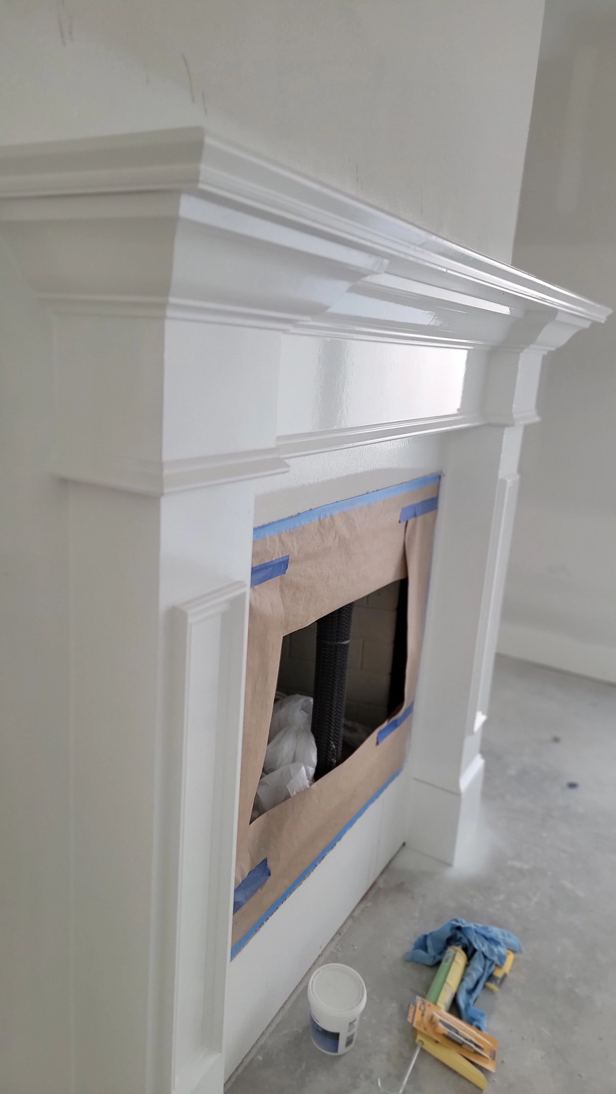 Partially painted white fireplace mantel with blue painter's tape and brown paper covering the opening, indicating ongoing painting or renovation work.