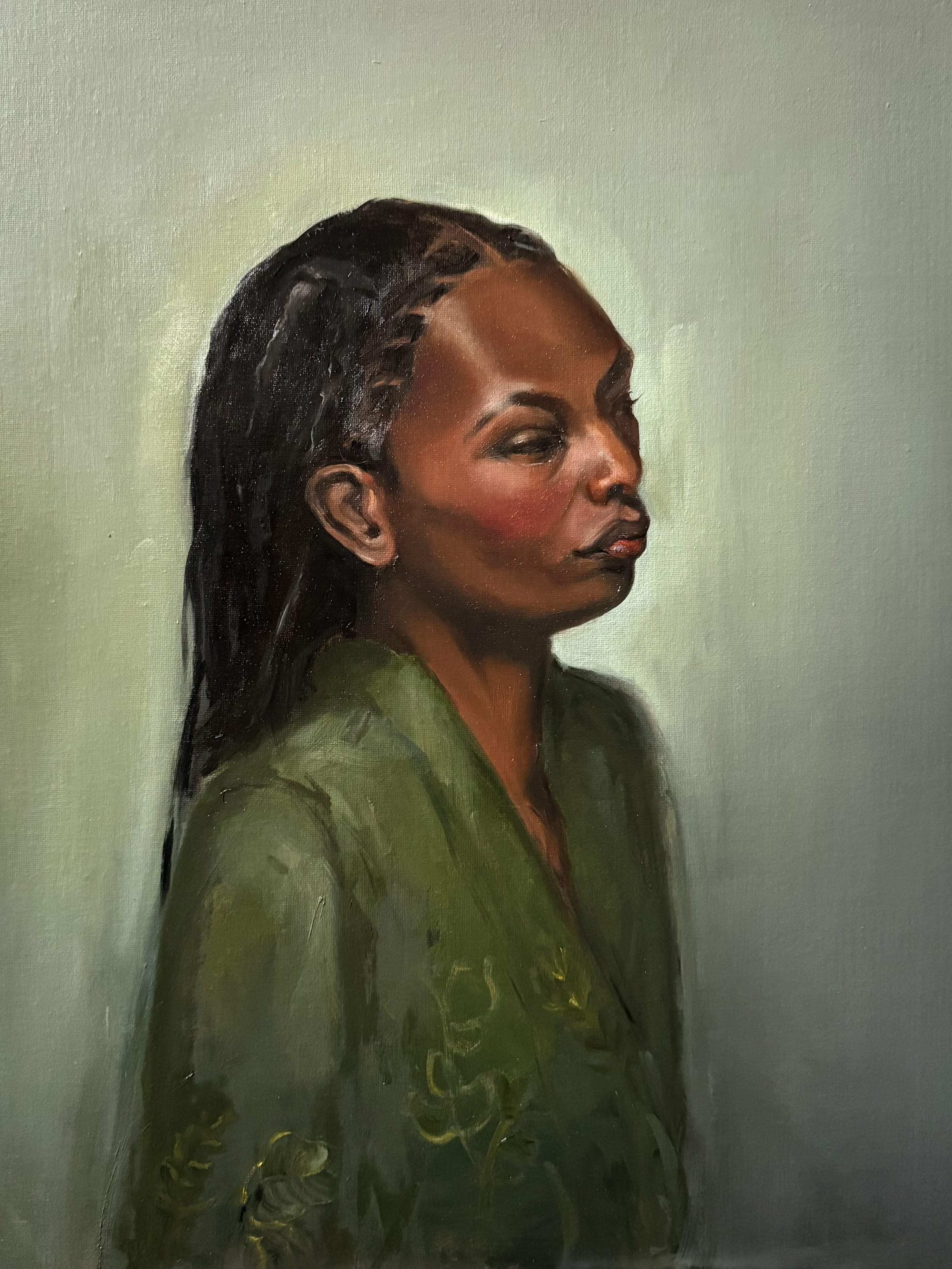 Portrait of a woman with dark hair styled with braids, wearing a green shirt, against a plain background.