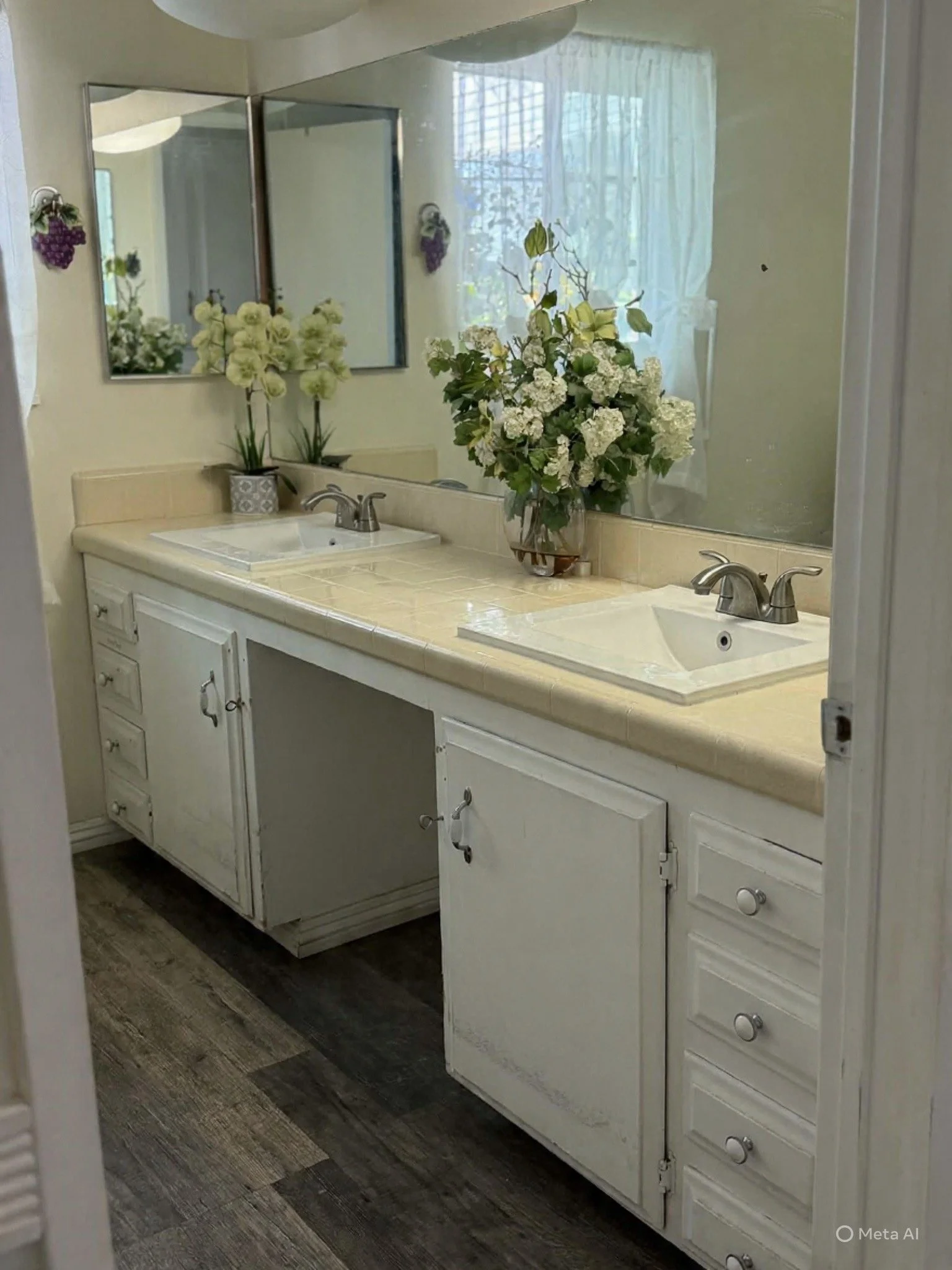 Bathroom with double sinks, large mirror, floral decorations, and window with curtains
