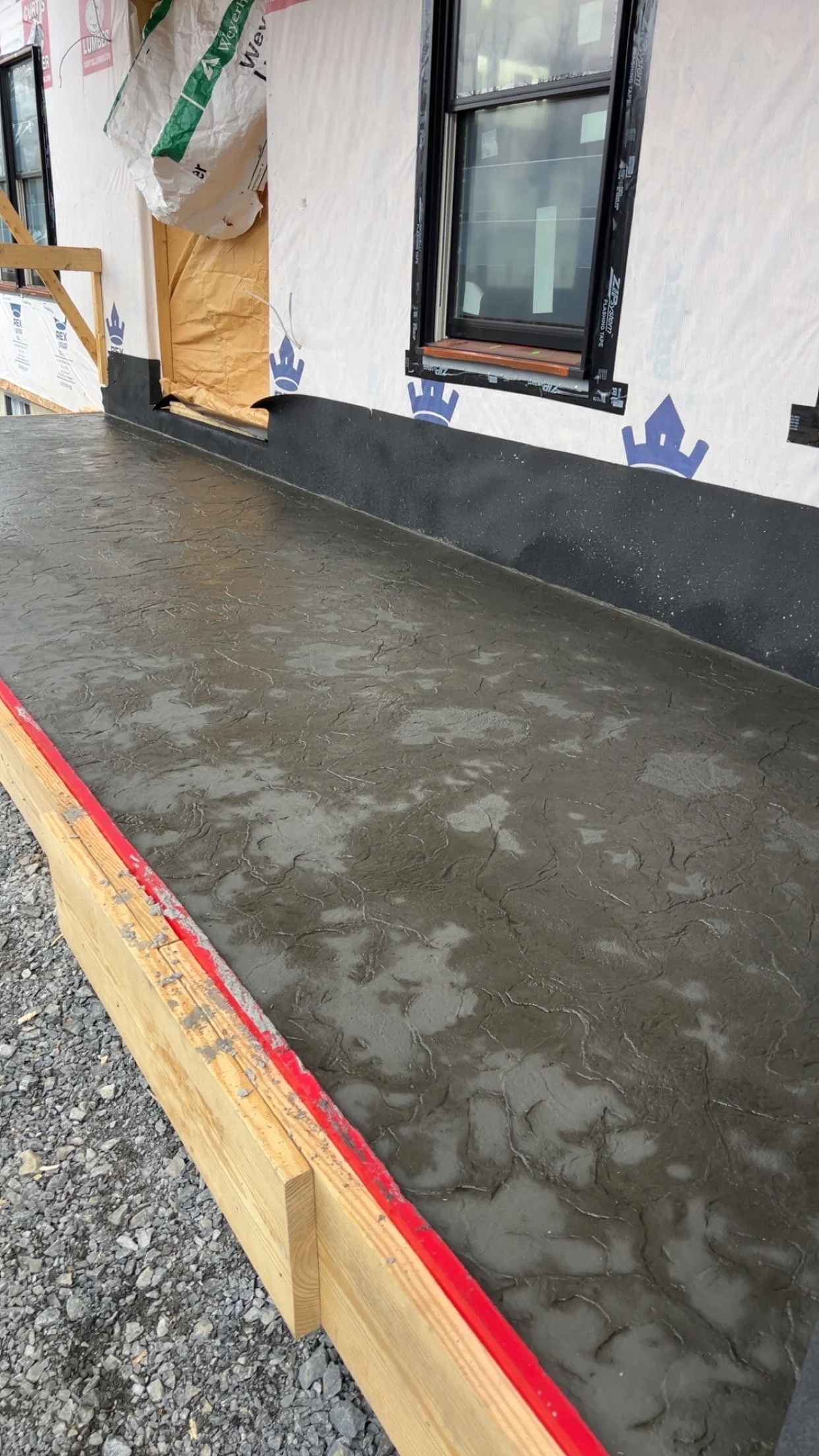 Freshly poured concrete slab outside a building under construction, with a window and partially finished wall visible in the background.
