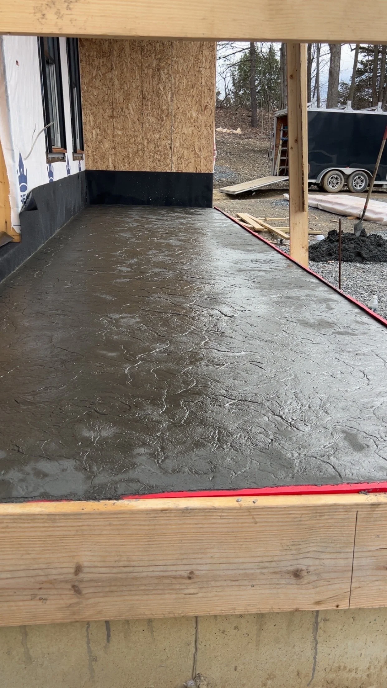 Freshly poured concrete slab with textured surface on a building under construction, surrounded by wood framing and construction materials.