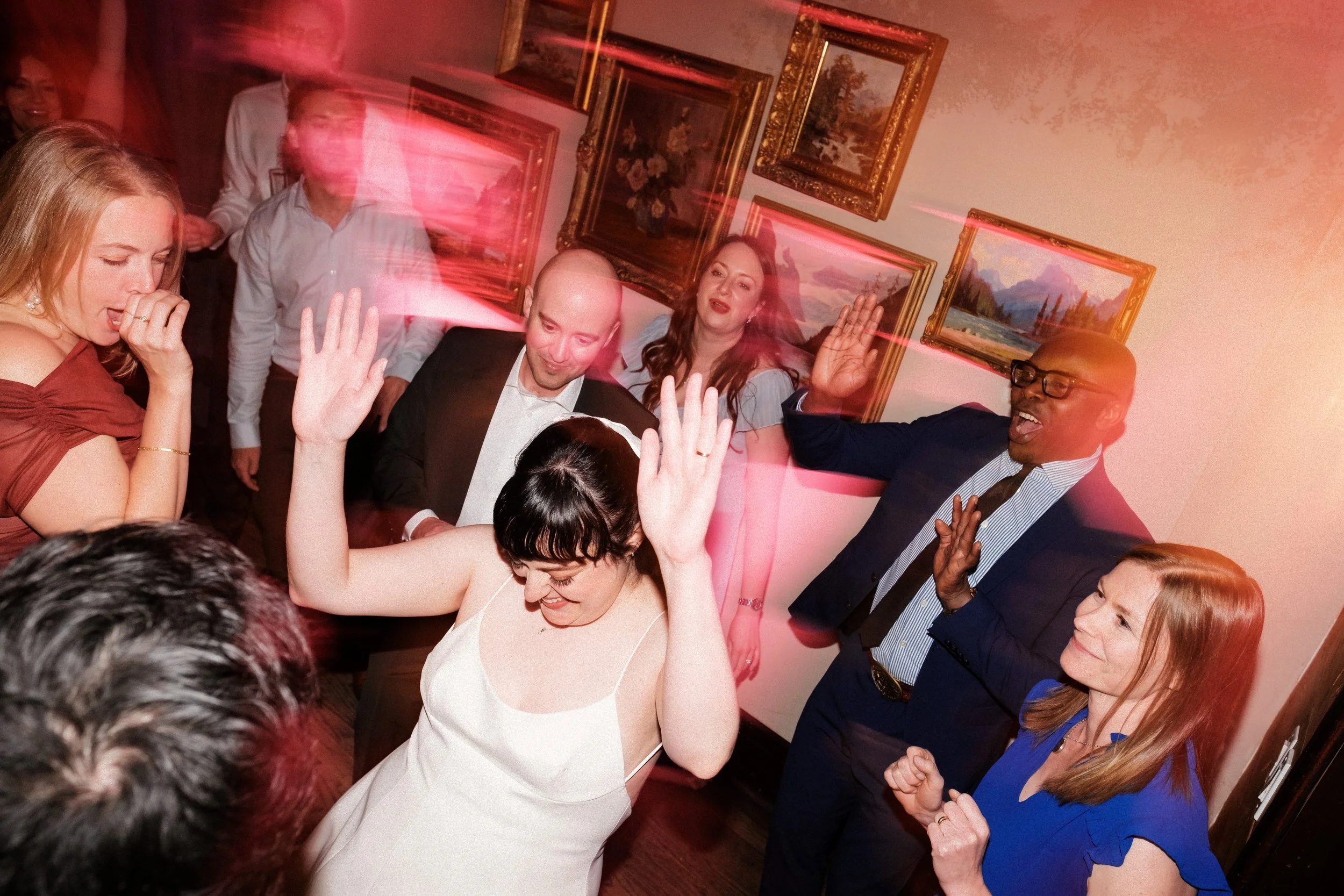 Group of people dancing and celebrating at a party, with some raising hands and smiling.