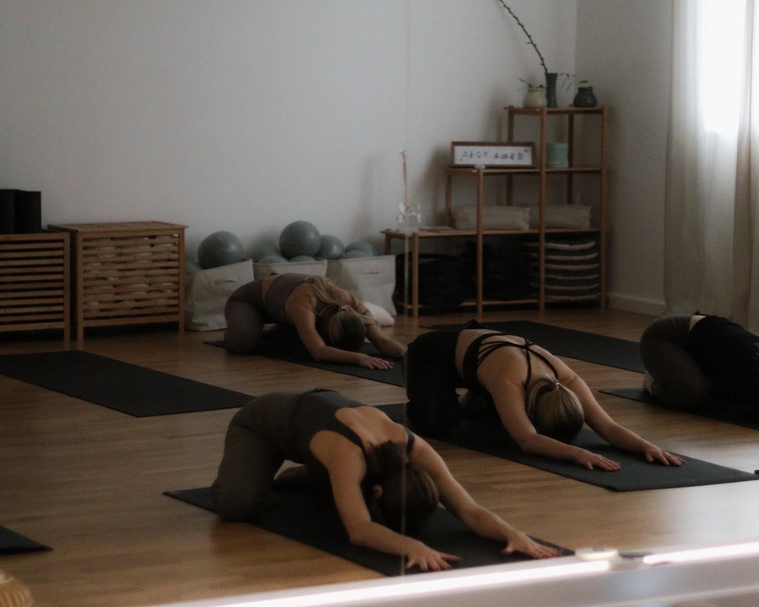 People practicing yoga in a dimly lit studio, doing child's pose on black mats.
