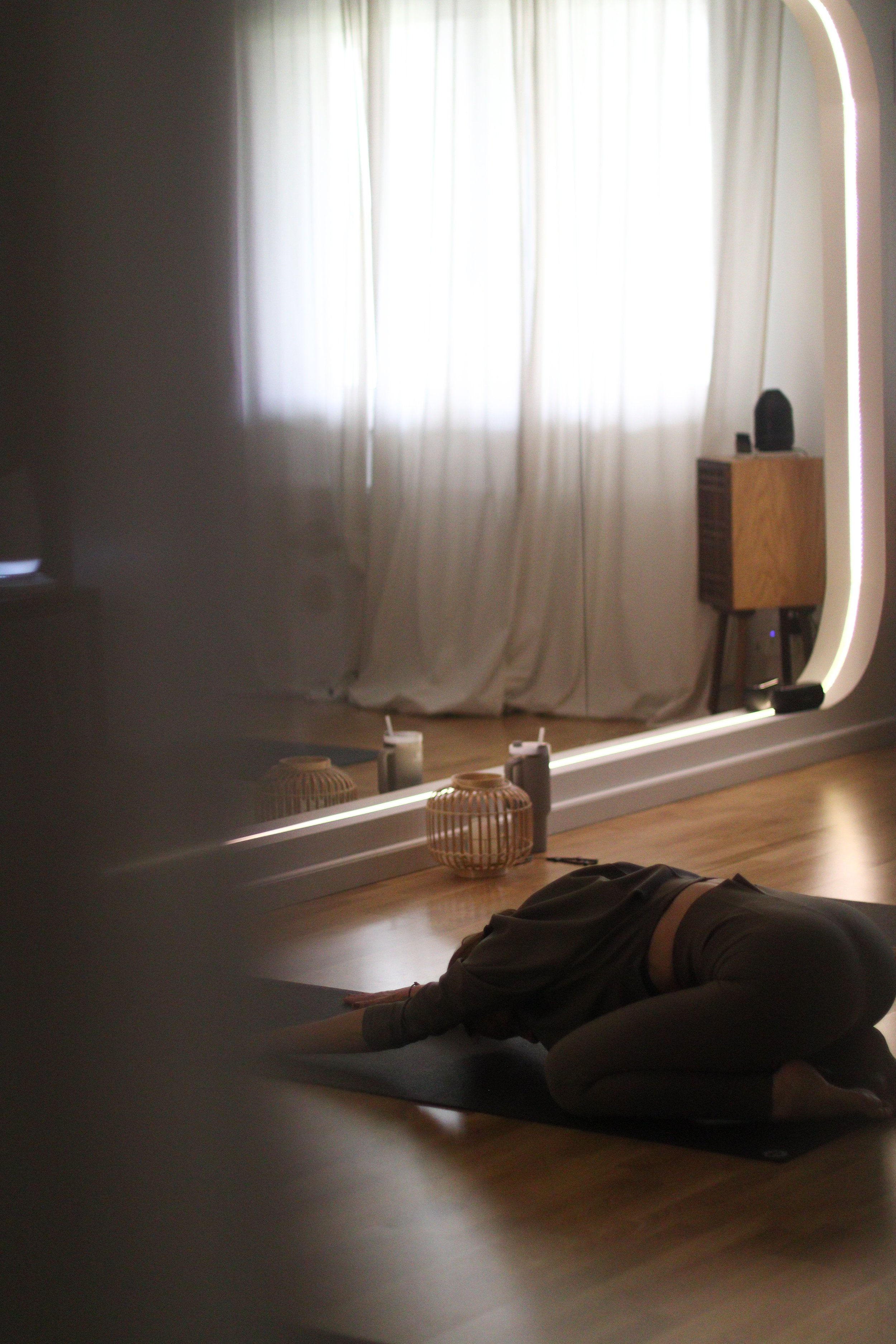 Person practicing yoga on a mat in a dimly lit room with curtains, candles, and a mirror.