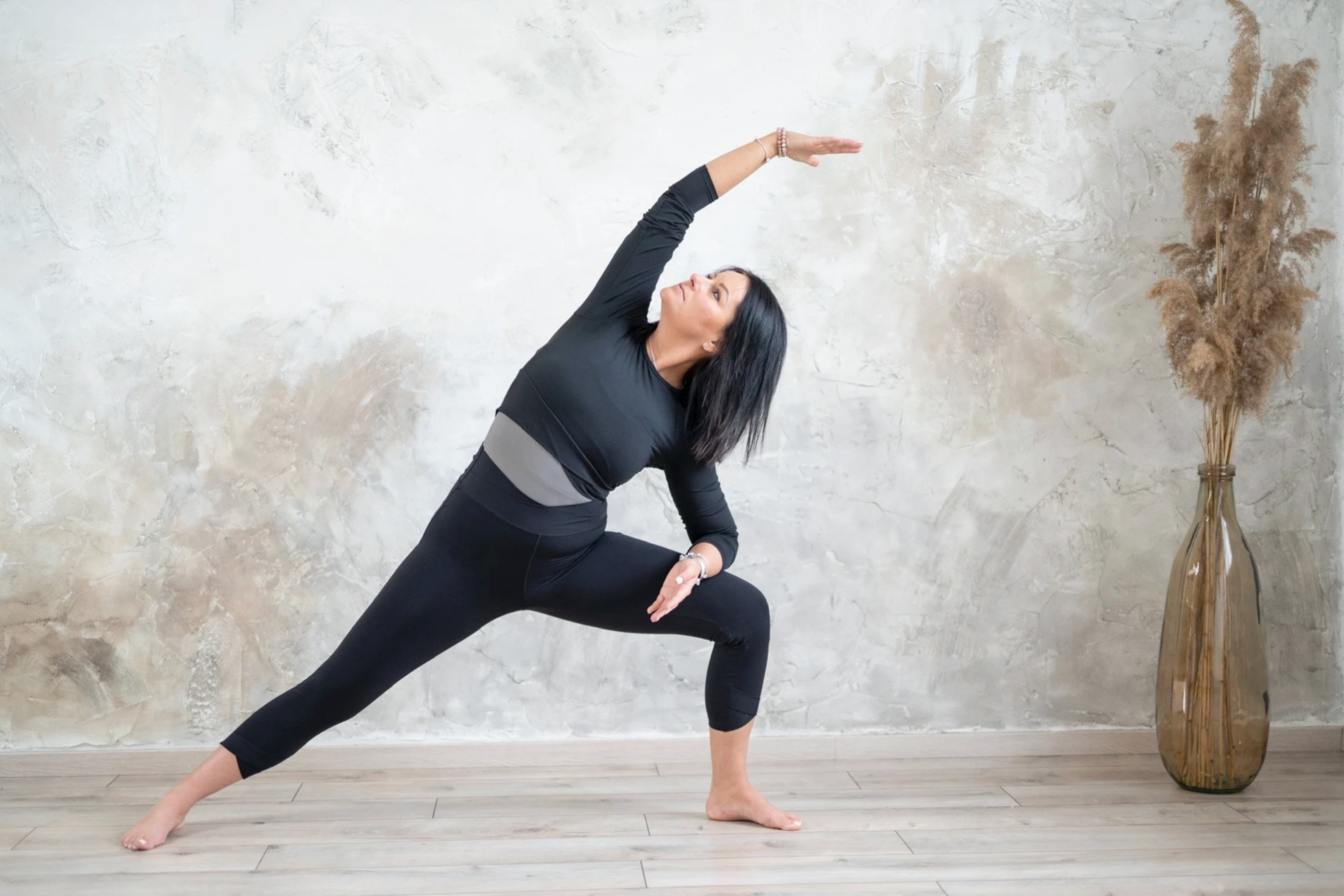 Woman in black workout clothes practicing yoga in a lunge position with her left knee bent and right leg extended behind her, reaching her right arm overhead and left arm across her body.