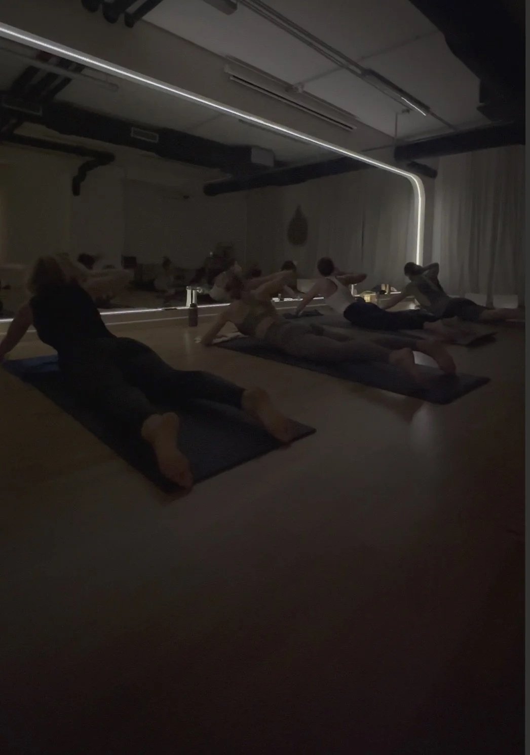 People practicing yoga in a dimly lit studio with a backlit mirror and minimal decor.