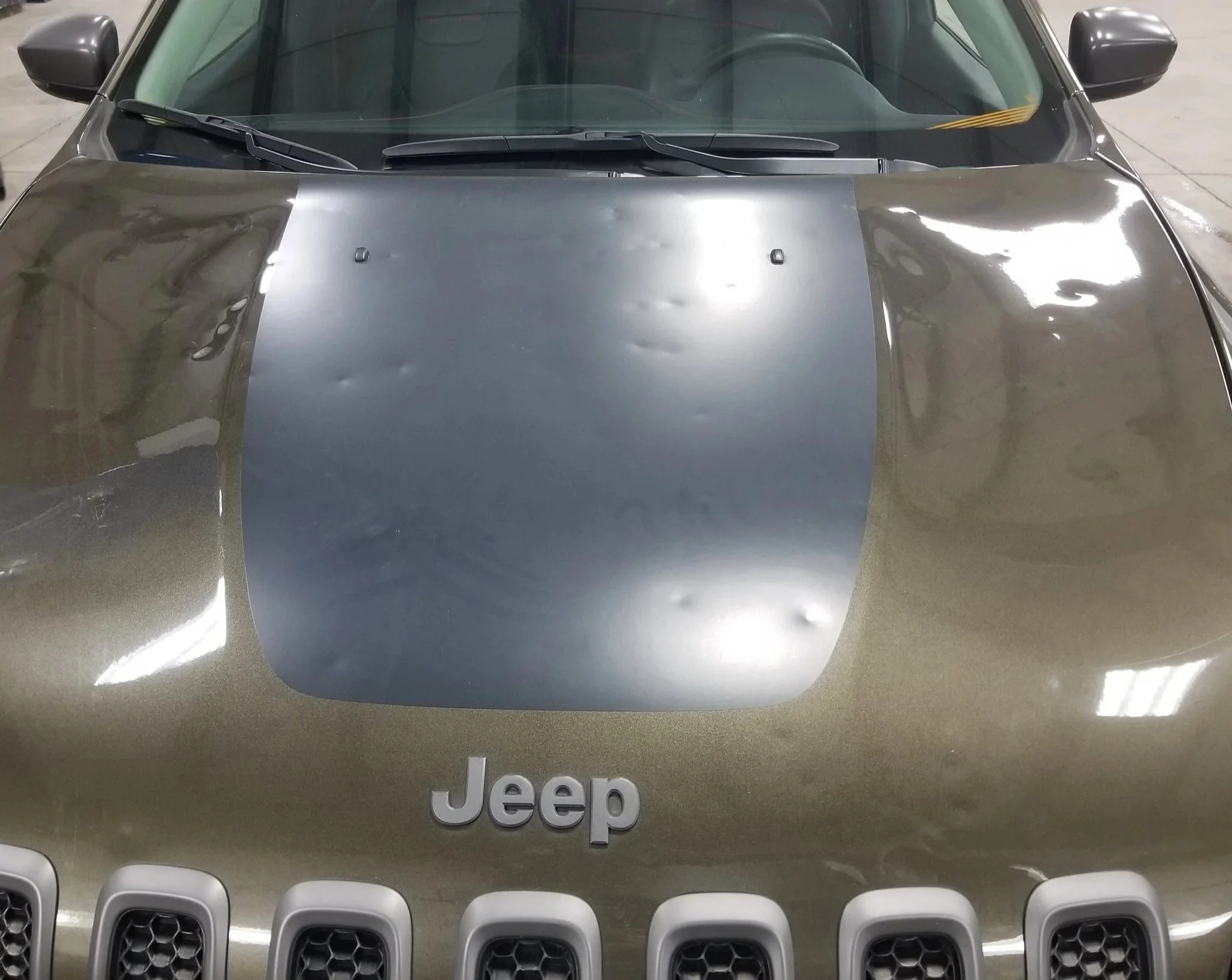 Front view of a beige Jeep vehicle with a black hood and the Jeep logo visible on the grille.