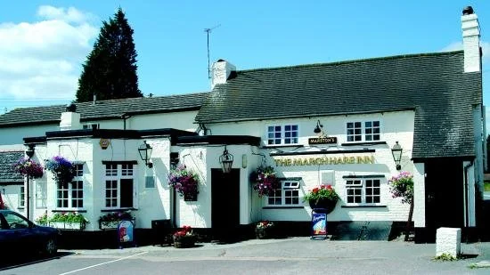 Exterior of The March Hare Inn with white walls, hanging flower baskets, and a sign above the entrance on a sunny day.