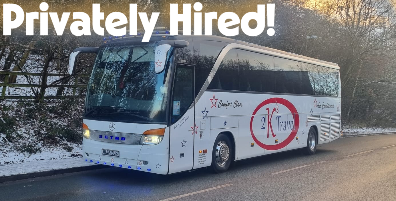 A white tour bus parked on the side of a road with snow on the ground and trees in the background. The bus has the words 'Privately Hired!' written across the top and features red and blue star decorations, with the logo '2K's Travel' prominently displayed on the side.