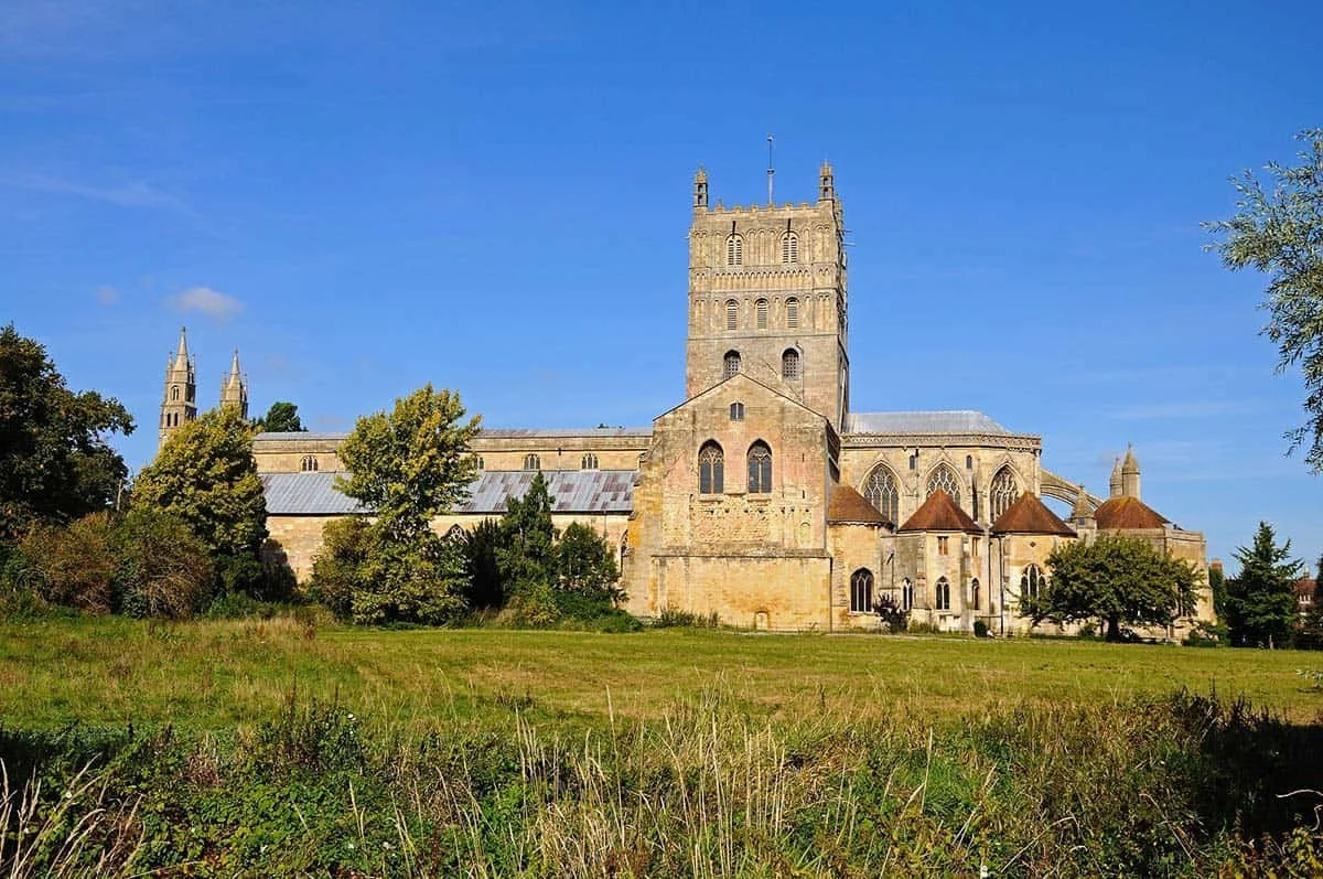 A large historic church or cathedral with tall towers and intricate architecture, surrounded by trees and a grassy field under a clear blue sky.