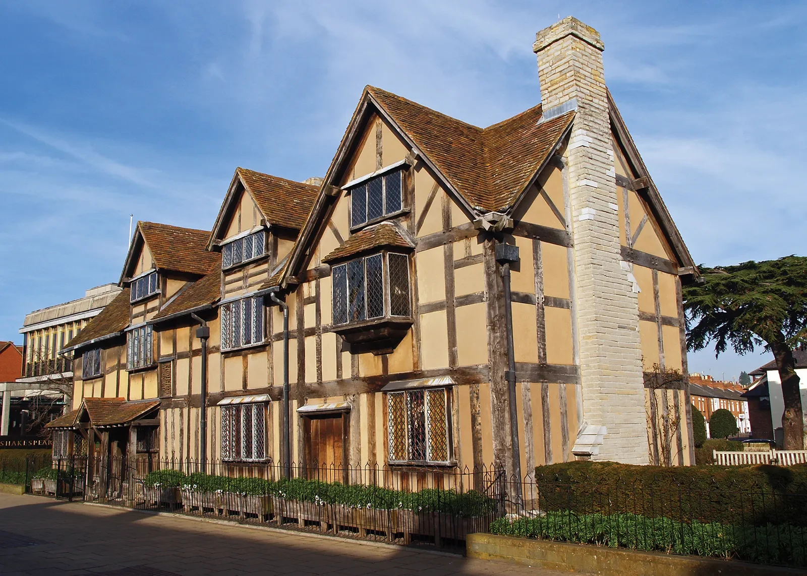 Historic half-timbered building with beige plaster walls, dark wooden beams, and leaded glass windows, located on a city street under a blue sky.