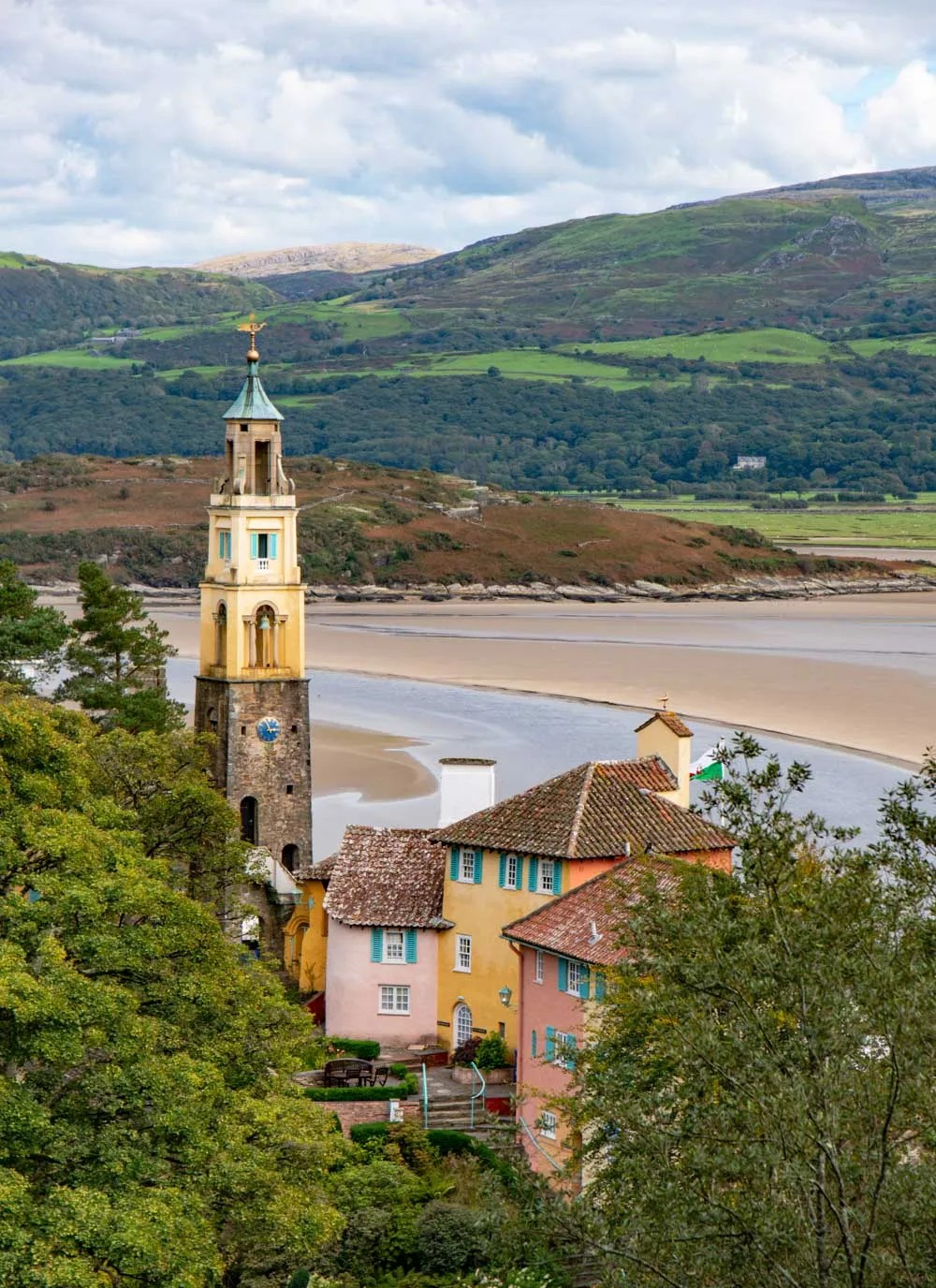 A colorful European-style town with pastel houses and a tall clock tower, set against a river and green hills in the background.